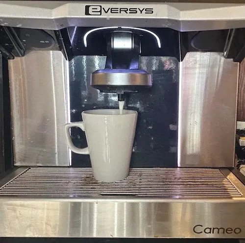 Front of an Eversys Cameo with the Eversys logo and Cameo lettering, milk pouring into a white mug
