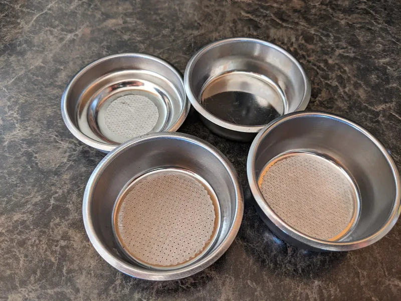 Quatre filtres espresso vus de dessus, simples et doubles, avec des zones perforées de tailles différentes