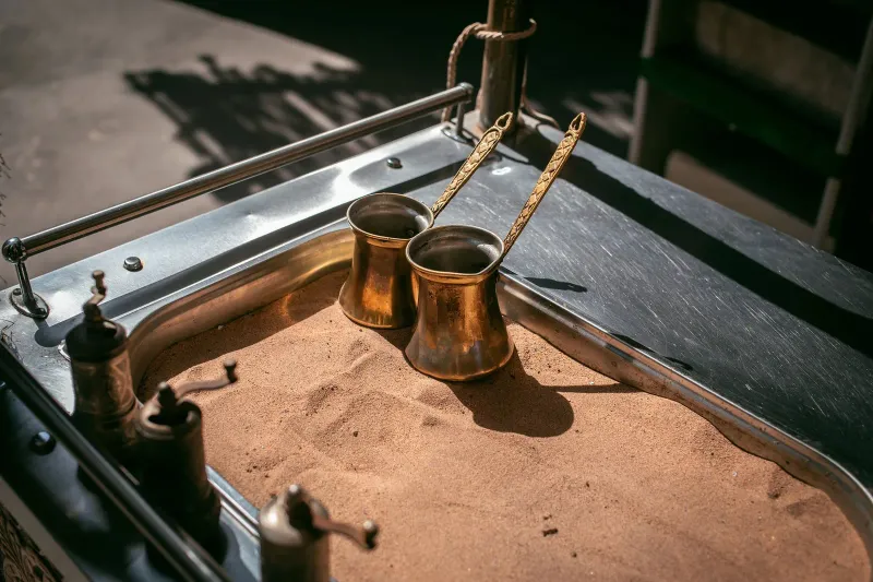 Zwei kupferne Cezve-Kännchen, halb in einer Schale mit heißem Sand vergraben, an einem Marktstand