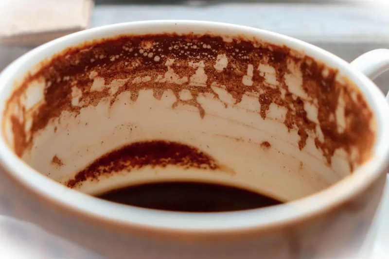 Leere Kaffeetasse auf ihrer Untertasse, innen mit dunklem Kaffeesatz überzogen, der am Porzellan herabläuft