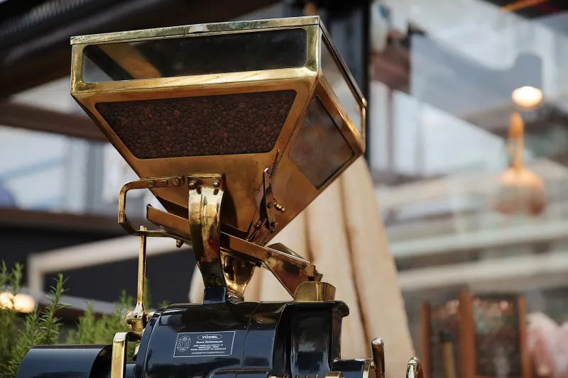 Hohe, reich verzierte Handmühle aus Messing mit einem kleinen Häufchen fein gemahlenen Kaffees darunter